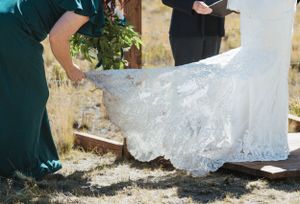 Someone adjusts the train of a white lace wedding dress outdoors on a sunny day.