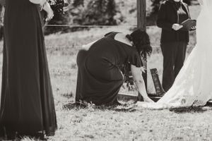 A black and white photo showing someone adjusting the hem of a wedding dress outdoors.
