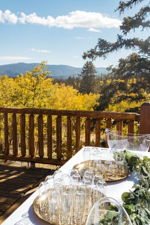 Champagne glasses set on white tablecloth with mountain vista and golden aspen trees from deck railing.