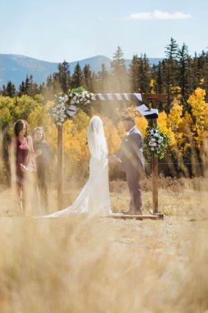 Outdoor mountain wedding ceremony with floral arch and golden fall foliage.