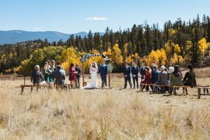 Wedding guests gathered in a mountain meadow with golden aspens and evergreen trees in the background.