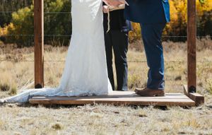 Wedding couple standing on wooden platform showing dress and formal shoes.
