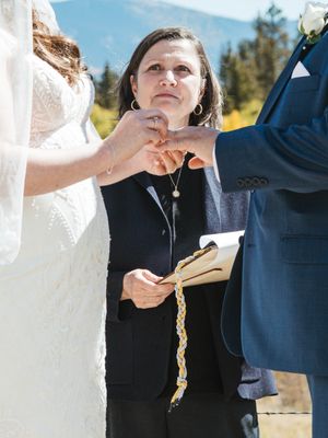 An outdoor wedding ceremony shows hands being joined together while an officiant holds a book.