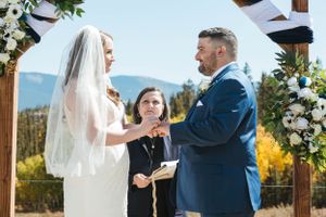 Wedding ceremony taking place outdoors with mountain views and floral arch decorations.