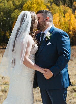 A romantic wedding kiss moment captured against a backdrop of golden fall foliage.