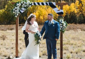 Wedding ceremony under a floral arch with fall foliage and mountains in the background.