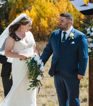 A wedding couple sharing a joyful moment against vibrant fall foliage.
