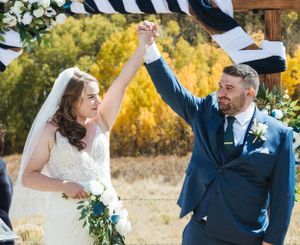 A joyful wedding couple celebrating with raised hands during their outdoor autumn ceremony.