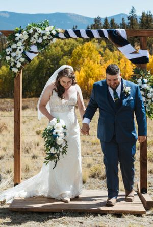 Wedding ceremony arch decorated with white flowers and black and white stripes against mountain backdrop.