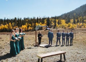 Outdoor wedding ceremony setup with wedding party in emerald green and navy against autumn colors.