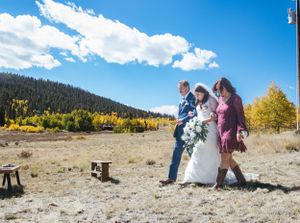 A small group walks across an open mountain meadow with golden aspens and blue skies.