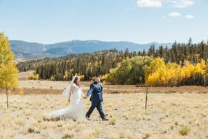 A couple walks hand in hand through a golden meadow with mountain views and autumn colors in the background.