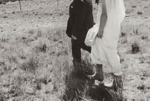 Black and white photo of boots and dress hem on desert terrain.