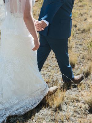 A close-up view of a bride in a lace wedding dress holding hands with someone wearing a navy blue suit.