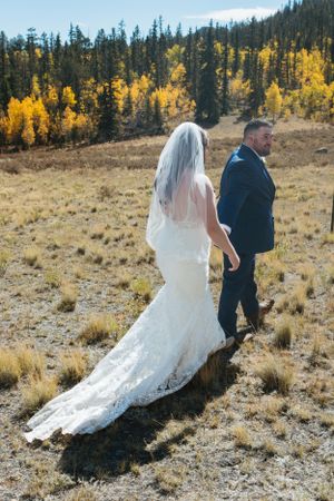 A wedding couple walks through an autumn mountain meadow with golden aspens in the background.