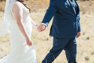 Close-up of wedding couple holding hands while walking in a rustic outdoor setting.