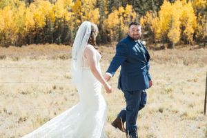 A couple walks through a mountain meadow with vibrant fall colors in the background.