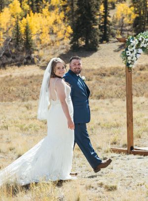 A newlywed couple poses playfully in front of autumn aspens with a floral wedding arch.