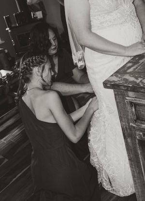 A black and white image shows final dress adjustments being made before a wedding ceremony.