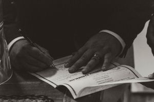 Black and white image of hands signing a document or certificate.