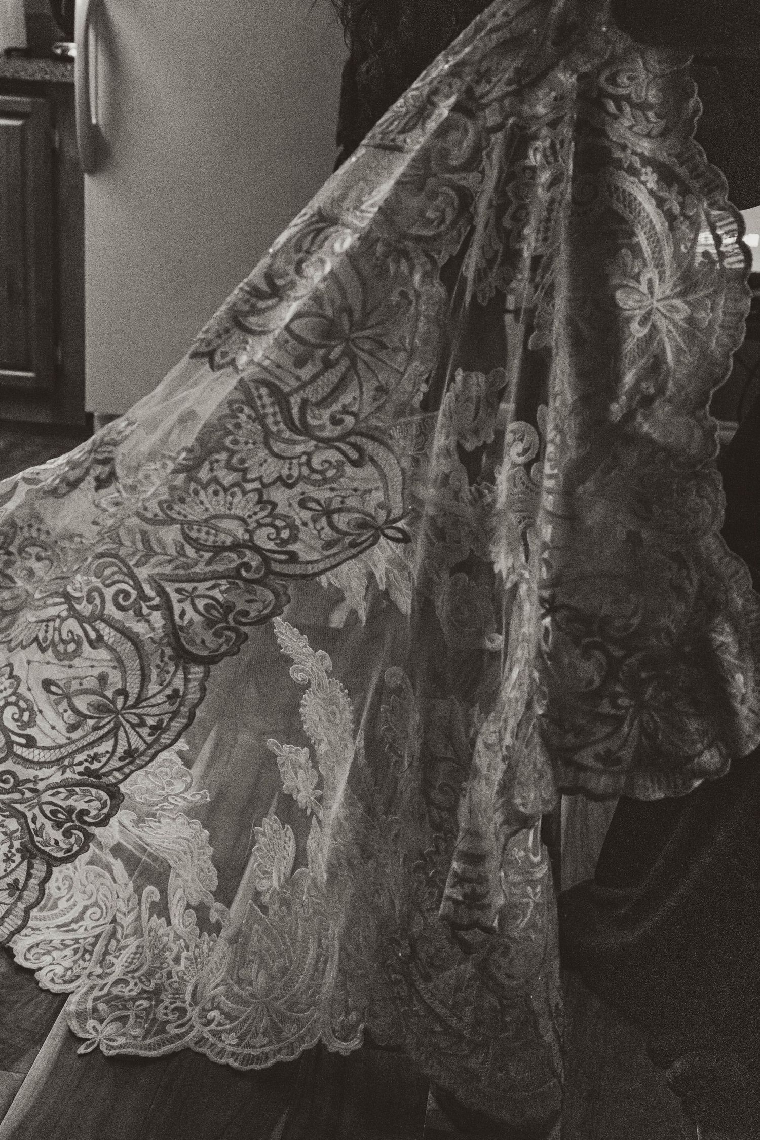 Detailed black and white photograph of intricate lace wedding dress fabric with floral patterns.