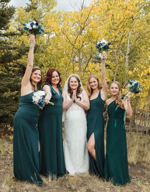 Bridesmaids in emerald green dresses celebrating with the bride against golden autumn trees.