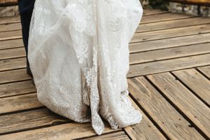 Close-up view of an elegant white lace wedding dress hem and train resting on wooden deck flooring.