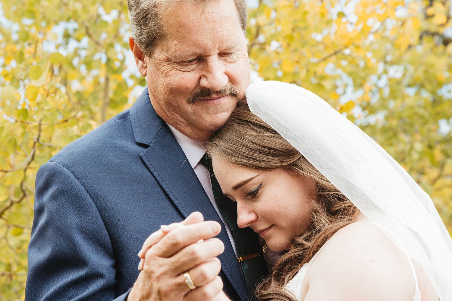 A tender moment between a couple on their wedding day with autumn foliage in the background.