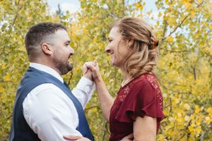 A couple shares a joyful moment outdoors with autumn foliage in the background.