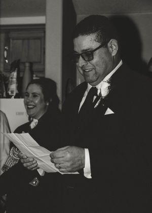 Guests at a formal event read papers while sharing a laugh in black and white photograph.