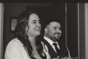 A black and white photo shows a couple laughing together, with the woman wearing white and the man in a dark suit.