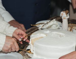 Hands cutting into a white wedding cake with decorative ornaments and figurines on top.