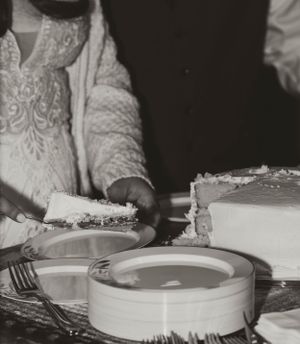 A black and white photograph showing hands serving slices of wedding cake on plates.