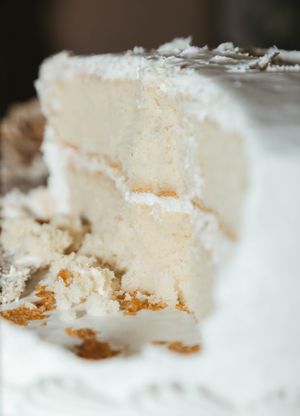 A slice of white wedding cake with layers of vanilla frosting and crumbs on a plate.