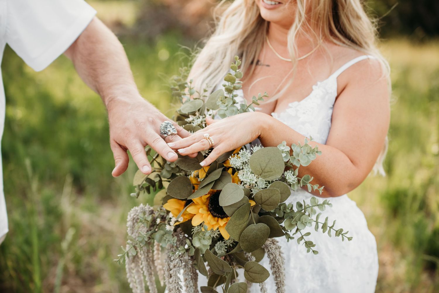 Close-up of hands holding a rustic wedding bouquet with eucalyptus and sunflowers.