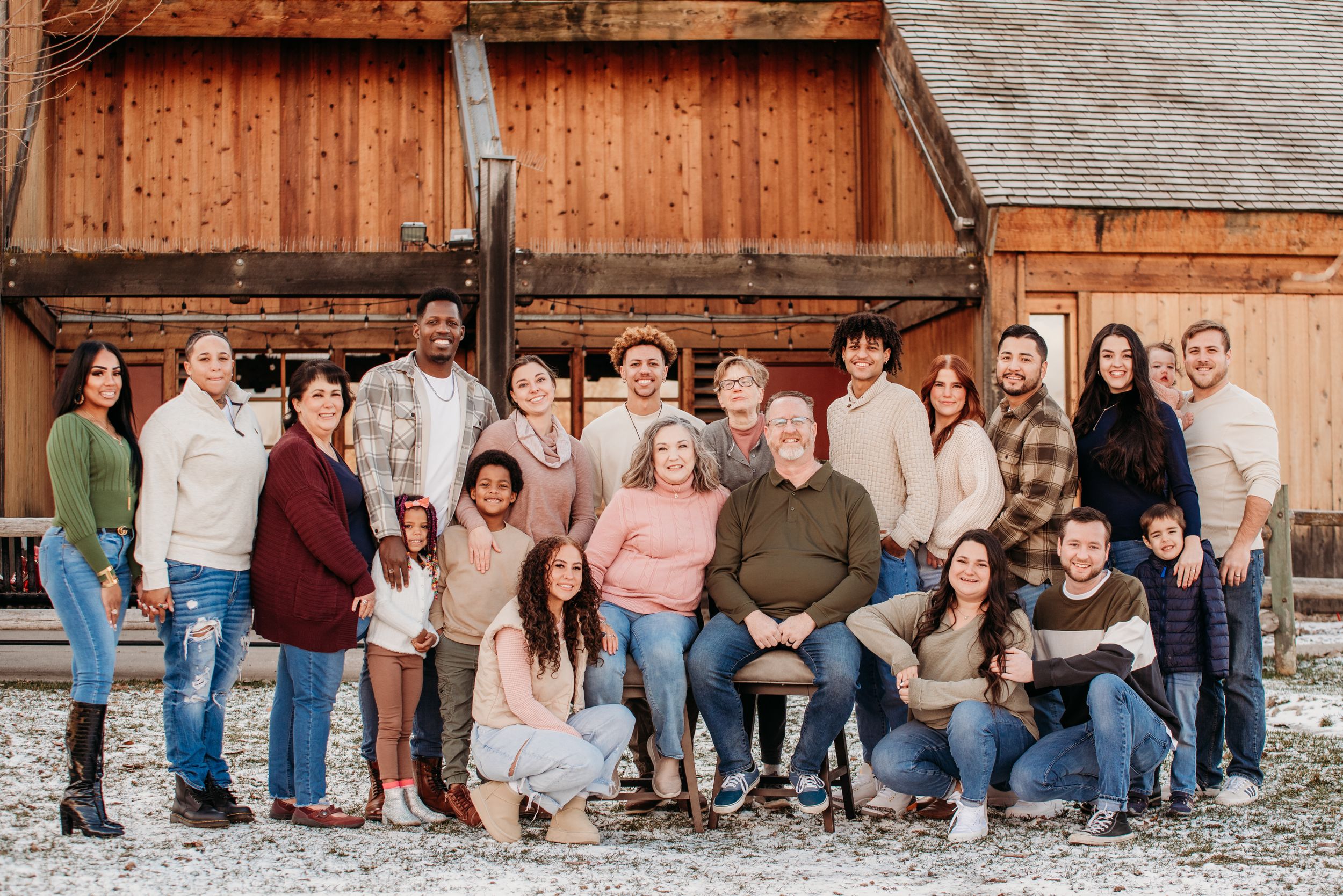 Large family group gathered in front of rustic wooden barn during outdoor portrait session.