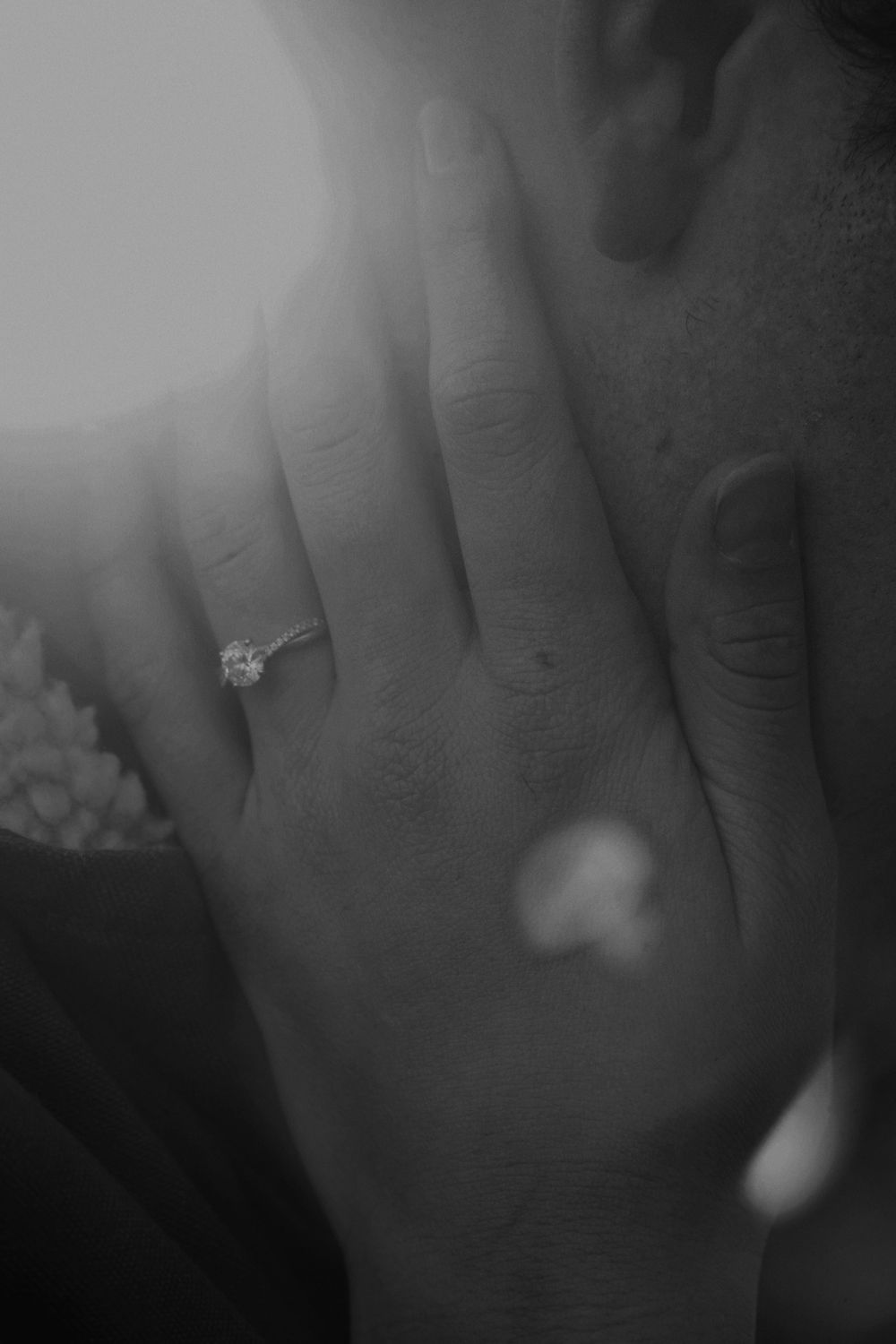 Black and white close-up of a diamond engagement ring on a woman's hand resting on a man's chest.