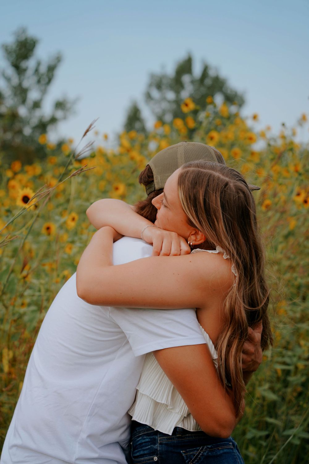 Couple sharing a warm embrace in a sunflower field under a blue sky.