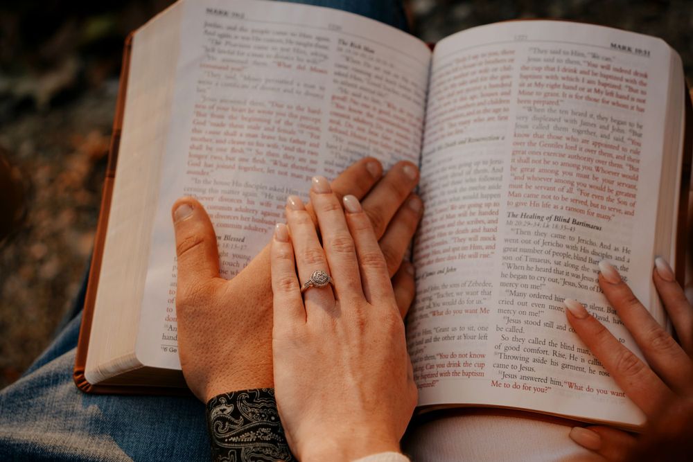 Couple's hands resting together on an open Bible, woman wearing a diamond engagement ring.
