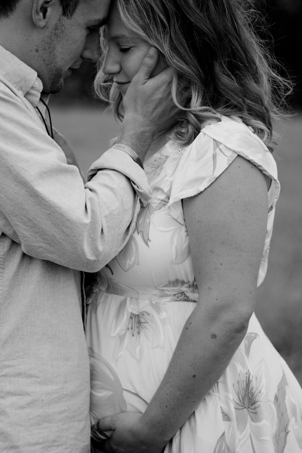 Black and white photo of a romantic couple embracing tenderly, man gently cupping pregnant woman's face in an intimate moment.