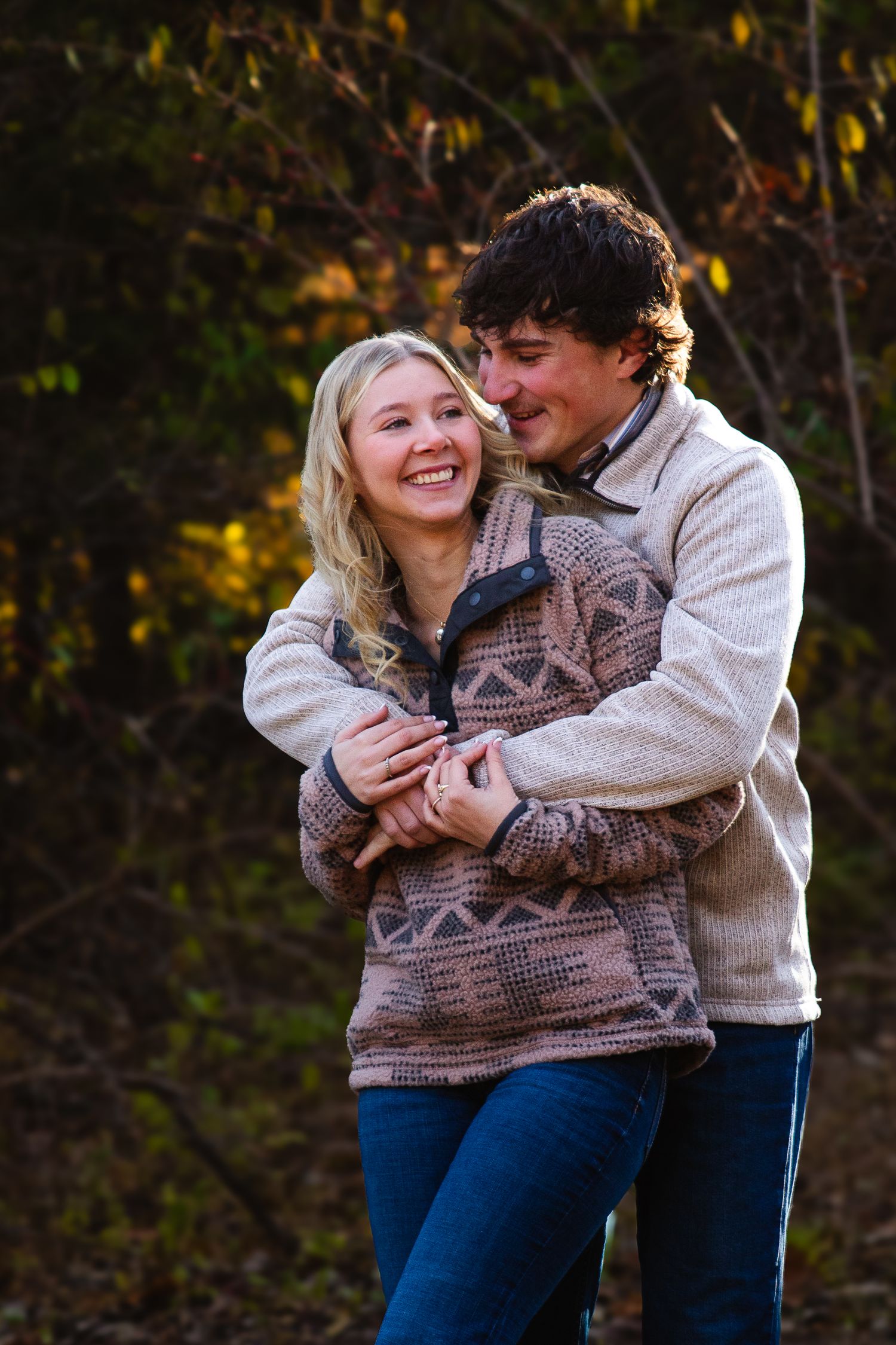Couple embracing and laughing while wearing cozy sweaters in an autumn setting.