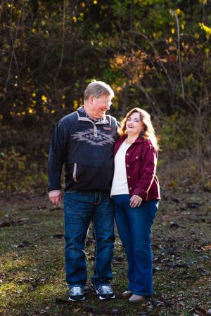 Couple shares a laugh while standing together on autumn forest trail.