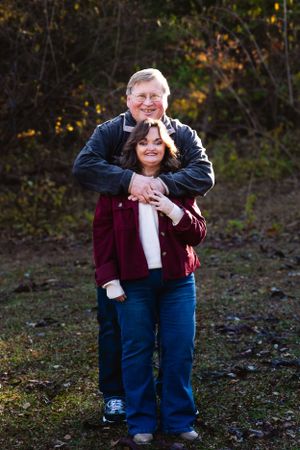 A warm embrace captured outdoors during autumn with burgundy and dark clothing against fall foliage.