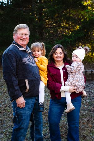 Family members pose together outdoors while holding two young children on a fall afternoon.