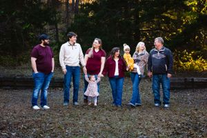 Family members arranged in a line pose together on a gravel path at dusk.