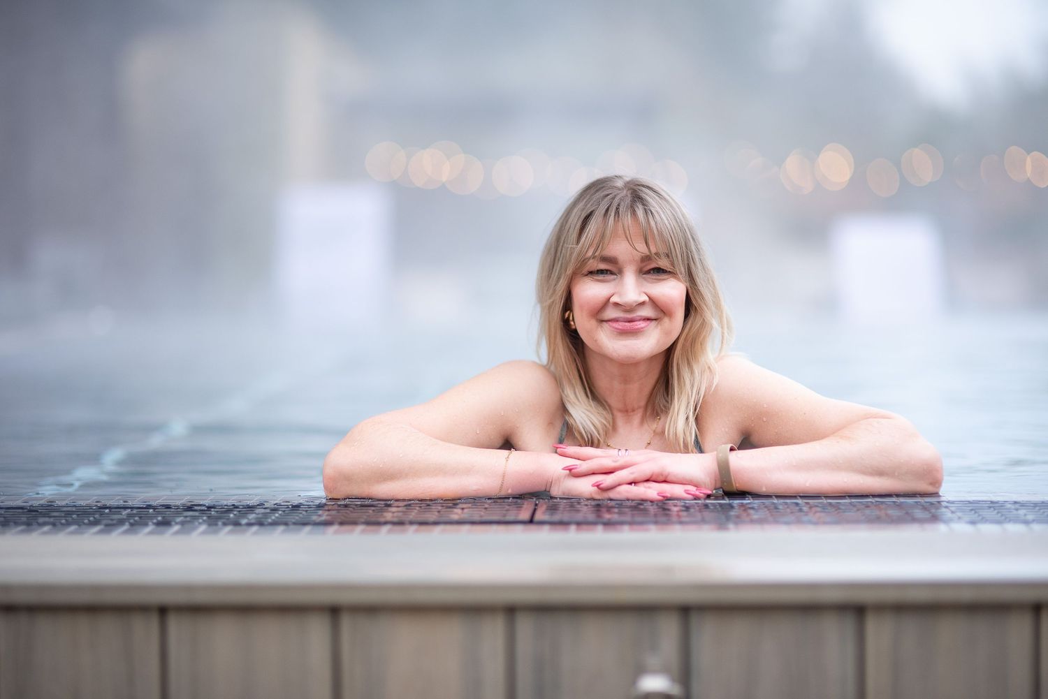 Person relaxing in a steamy outdoor hot spring or thermal pool on a misty day.