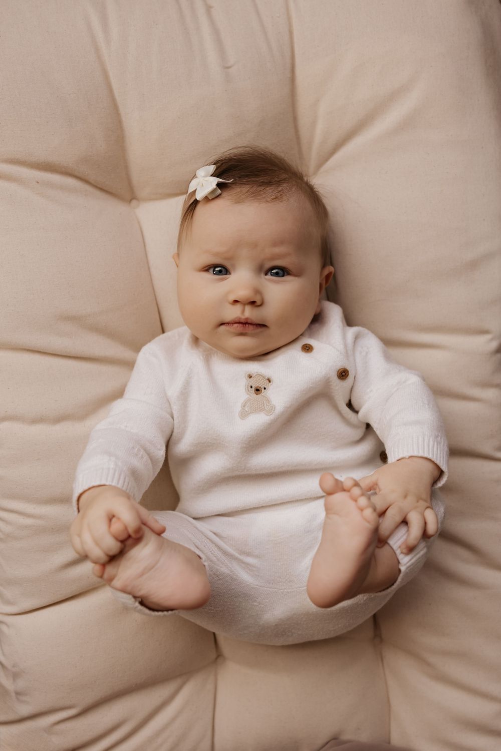 Baby wearing white sweater lying on cream colored cushions in a series of candid poses.