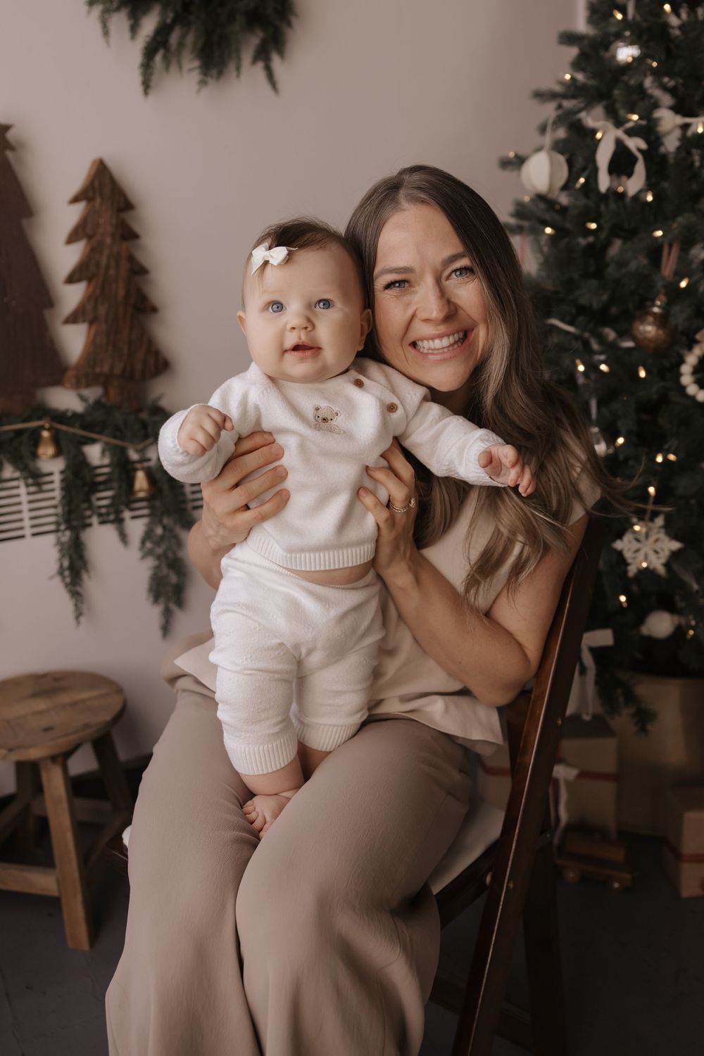 Holiday family photos with baby in white sweater against Christmas decor background.