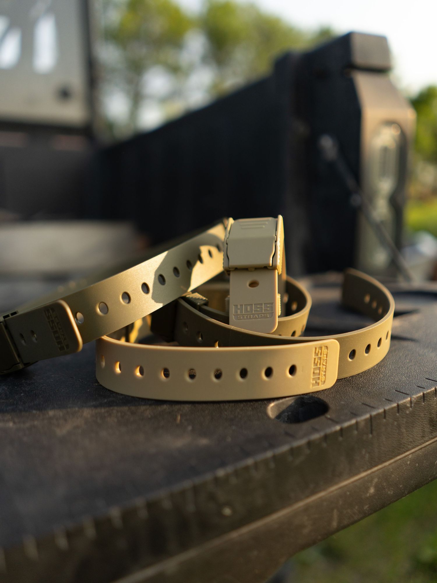 Tan tactical belt straps arranged on dark surface in natural lighting.
