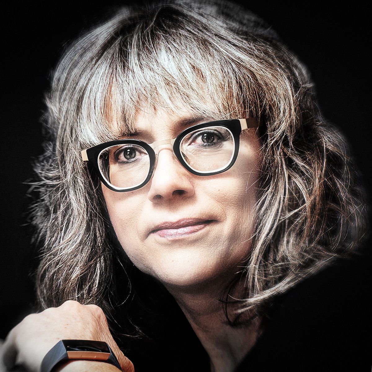 A person with silver-white hair and glasses smiles in a dimly lit setting, shown in a series of similar selfie poses.